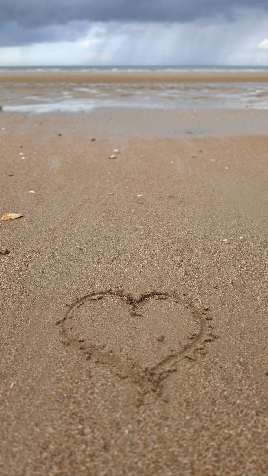 Zwei ineinander gezeichnete Herzen im Sand am Meer – Symbol für Verbundenheit zwischen Menschen.
